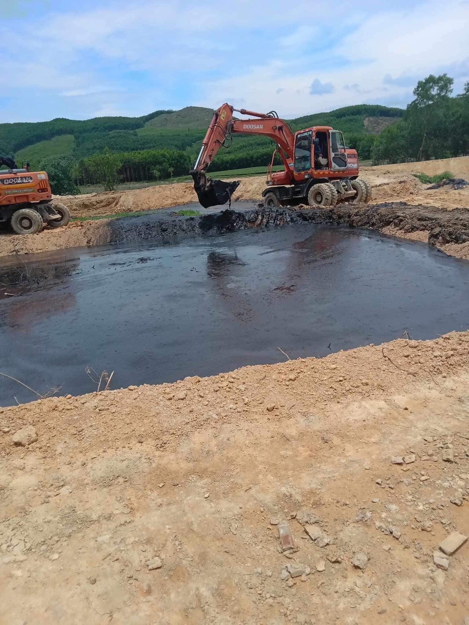 Dùng máy đào đất đổ vào bể chứa phân lợn gây mùi hôi thối nên người dân tập trung phản đối