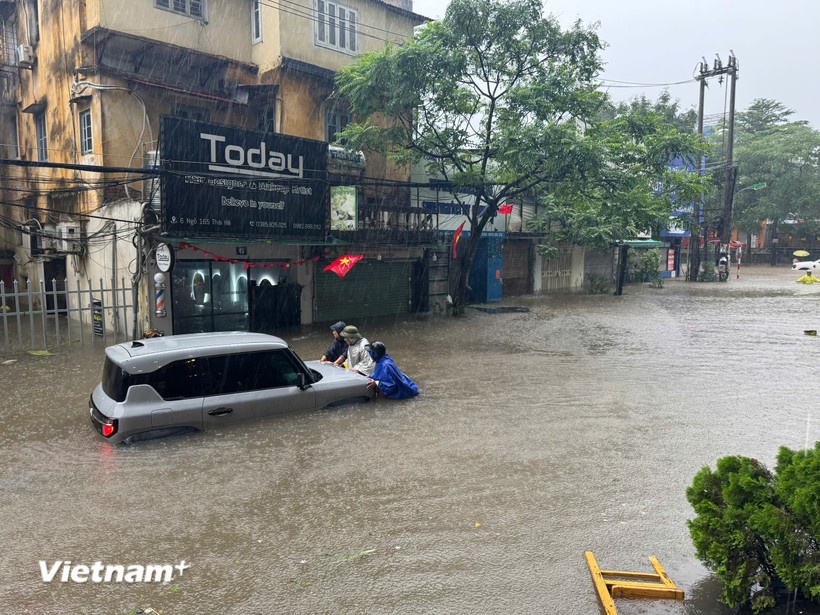 Người dân cố gắng đẩy phương tiện chết máy tới chỗ cao ráo hơn. (Ảnh: Vietnam+)